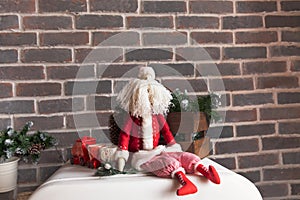 Christmas decorations, a toy Santa with a white beard sits against a brown brick wall.