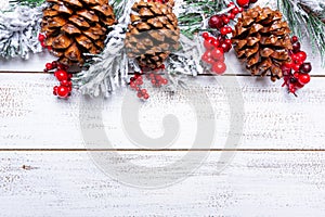 Christmas decorations on a white wood background with copy space. Pine cones, garland, berries and pine branches