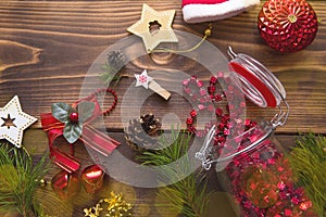 Christmas decorations on a wooden background. Beads in a glass jar with a lid, stars, Santa hat, cones, pine branches. New year, p