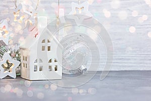 Christmas decorative house, glass balls and garland lights on white wooden background