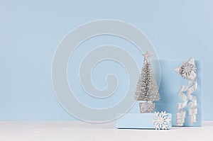 Christmas decorative silver tree with gifts and ribbons on white wood table and pastel blue wall.