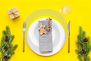 Christmas dinner decoration with gift box, plate and fir tree yellow table background top view