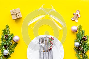 Christmas dinner decoration with gift box, plate and fir tree yellow table background top view