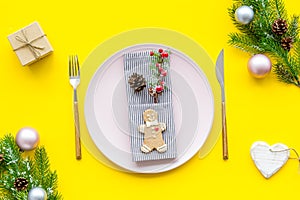 Christmas dinner decoration with gift box, plate and fir tree yellow table background top view