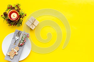 Christmas dinner decoration with gift box, plate and fir tree yellow table background top view mock-up
