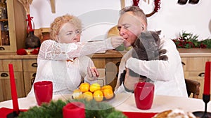 Christmas dinner at home with tangerine. Senior couple sitting at table in kitchen, eating tangerines.