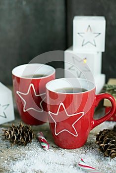 Christmas drink.Tea or coffee in red mugs on wooden table with candy cane.