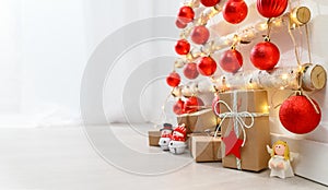 Christmas eco tree made of wooden branches hanging on white wall with festive lights and gift boxes on the floor.