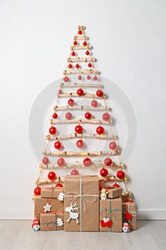 Christmas eco tree made of wooden branches hanging on white wall with festive lights and gift boxes on the floor.