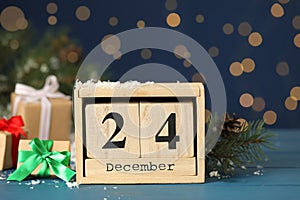 Christmas Eve - December 24. Block calendar, gift boxes and fir tree branch on light blue wooden table