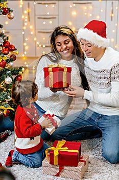 Christmas Eve gifts for all family members. Parents with their child at the Christmas tree in their new home.