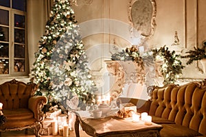 Christmas evening by candlelight. classic apartments with a white fireplace, decorated tree, sofa, large windows and