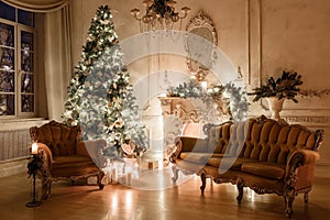 Christmas evening by candlelight. classic apartments with a white fireplace, decorated tree, sofa, large windows and