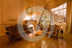 Christmas evening by candlelight. classic apartments with a white fireplace, decorated tree, sofa, large windows and