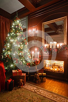 Christmas evening by candlelight. classic apartments with a white fireplace, decorated tree, sofa, large windows and