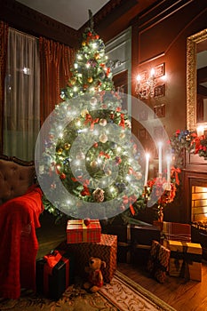 Christmas evening by candlelight. classic apartments with a white fireplace, decorated tree, sofa, large windows and