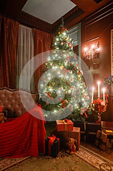 Christmas evening by candlelight. classic apartments with a white fireplace, decorated tree, sofa, large windows and