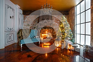 Christmas evening by candlelight. classic apartments with a white fireplace, decorated tree, sofa, large windows and