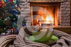 Christmas evening. Cozy fireplace and a cup of tea on wooden table, warm scarf