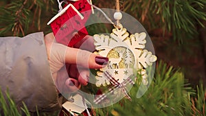 On Christmas evening, female hands straighten a snowflake on a green branch.