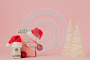 Christmas expenses. Pink leather purse with santa claus cap, gift, fir tree and dollars banknotes on pink background. Christmas