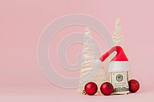 Christmas expenses. Pink leather purse with santa claus cap, gift, fir tree and dollars banknotes on pink background. Christmas