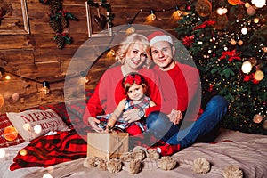 Christmas family with child smiling near the Xmas tree. Living room decorated by Christmas tree and present gift boxes