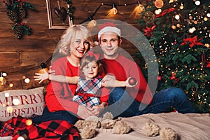 Christmas family with child smiling near the Xmas tree. Living room decorated by Christmas tree and present gift boxes