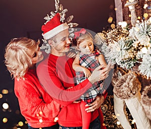 Christmas family with child smiling near the Xmas tree. Living room decorated by Christmas tree and present gift boxes, the ligh