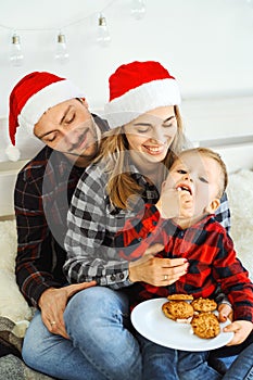 Christmas family in Christmas Santa hats. Dad, mom and son spending time together, eating cookies and hugs in the bed at