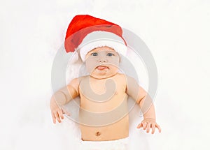 Christmas and family concept - cute funny baby in red santa hat lying on white bed home, humor, joke