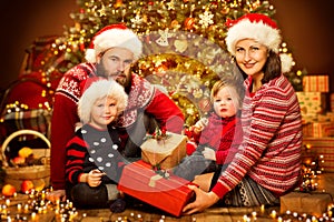 Christmas Family front of Xmas Tree Open Present Gift Box, Father Mother Child and Baby in Red hat