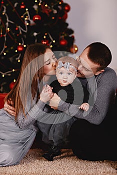 Christmas family kissing and hugging. Child surprised his mother and father with a Christmas gift. Family near christmas tree.