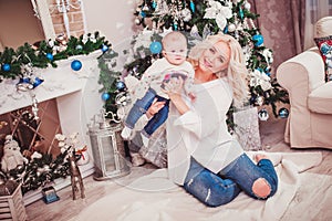 Christmas family, mother and baby smiling near the Xmas tree. Living room decorated by Christmas tree and present gift box