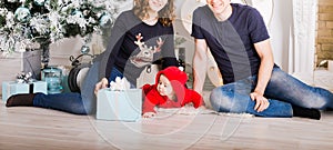 Christmas Family Open Present Gift Box, Mother Father and Baby Child in Decorated Room, sitting under Christmas Tree.