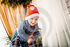 Christmas family portrait of happy smiling little boy in red santa hat in father`s hands. Winter holiday Xmas and New Year concept