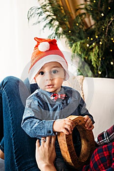 Christmas family portrait of happy smiling little boy in red santa hat in mother`s hands. Winter holiday Xmas and New Year concept