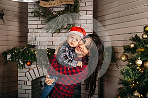 Christmas family portrait of happy smiling little boy in red santa hat in mother`s hands. Winter holiday Xmas and New Year concept