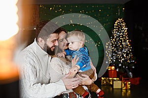 Christmas Family Portrait In Home Holiday Living Room. Parents with little son in arms standing near beautiful Christmas