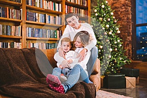 Christmas family portrait. Young Caucasian family in identical clothes having fun on sofa in living room with large library of