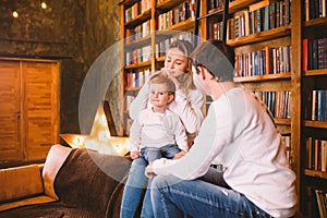 Christmas family portrait. Young Caucasian family in identical clothes having fun on sofa in living room with large library of