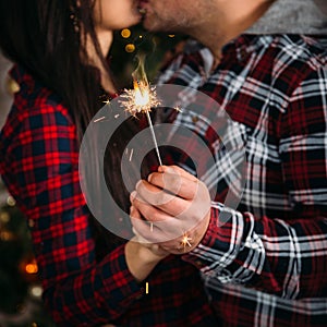 Christmas family portrait of young couple kissing and holding sparklers. Winter holiday Xmas and New Year concept