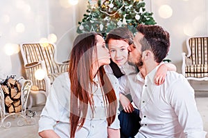 Christmas family smiling and kissing near the Xmas tree. Living room decorated by Christmas tree and present gift box