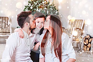 Christmas family smiling and kissing near the Xmas tree. Living room decorated by Christmas tree and present gift box