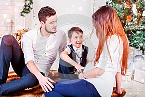 Christmas family smiling and kissing near the Xmas tree. Living room decorated by Christmas tree and present gift box