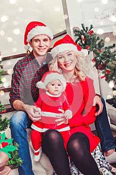 Christmas family smiling near the Xmas tree. Living room decorated by Christmas tree and present gift box