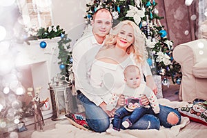 Christmas family smiling near the Xmas tree. Living room decorated by Christmas tree and present gift box