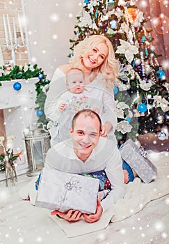 Christmas family smiling near the Xmas tree. Living room decorated by Christmas tree and present gift box