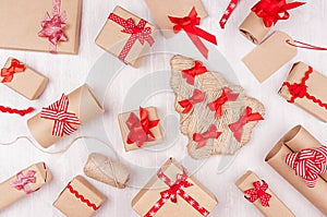Christmas festive background - different gifts boxes of kraft paper, blank labels and red ribbons, bows on soft white wood board.