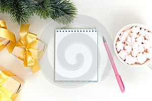 Christmas festive composition. White notepad, pink pen, gifts with a gold bow on a light table. Flat lay, top view